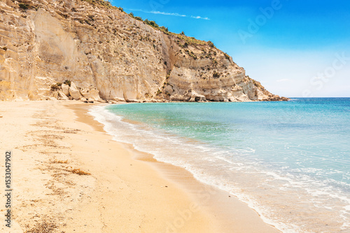 Fototapeta Naklejka Na Ścianę i Meble -  Calm turquoise water gently washing sandy shore with white cliff towering in background
