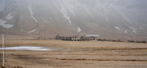 Houses standing on vast plain at foot of mountain with fog rolling in. Icelandic landscape iceland