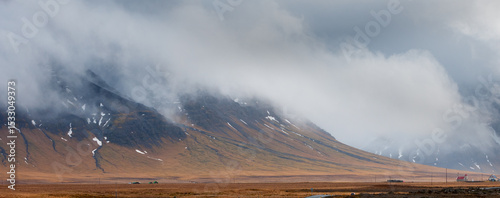 Low clouds covering majestic mountains in iceland with houses in the foreground
