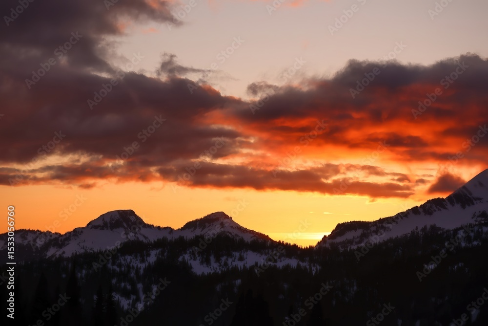 Obraz premium Sunset over snowy mountain peaks with orange and gray clouds filling the sky at dusk in a scenic view