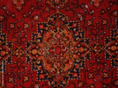 Red patterned oriental rug textile. Close-up of a richly designed red oriental rug with symmetrical floral ornaments and vintage texture.
