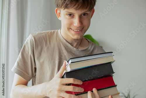 Portrait of a cheerful, cute, handsome, brown-eyed teenager boy with books in his hands, student with textbooks