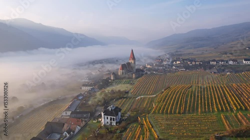 Aerial panorama of Weisenkirchen in der Wachau town and vineyards at autumn morning with fog over Danube river. Wachau valley, Austria.