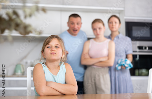 At home kitchen, parents scold daughter for careless act. Sulky preschool girl sit near table during serious conversation with parents