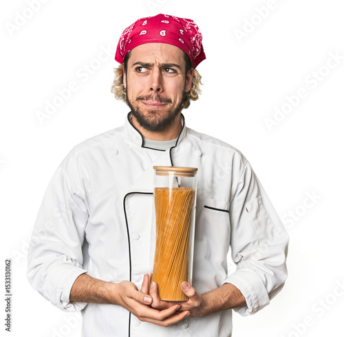 Young chef holds pasta sauce jar in studio confused, feels doubtful and unsure.