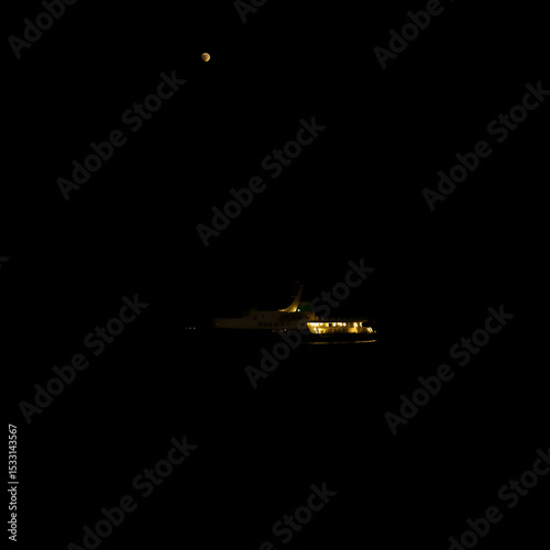 A large boat is sailing on a calm ocean at night. The sky is dark and the moon is visible in the distance. The scene is peaceful and serene, with the boat being the focal point of the image