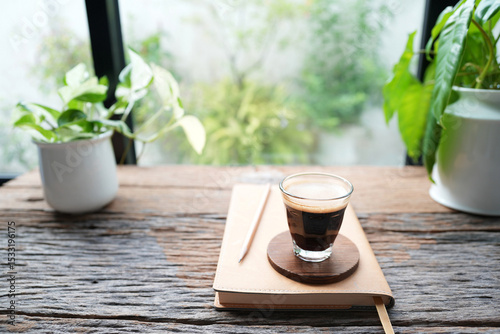 Coffee and brown small notebook on rustic wood table by the window