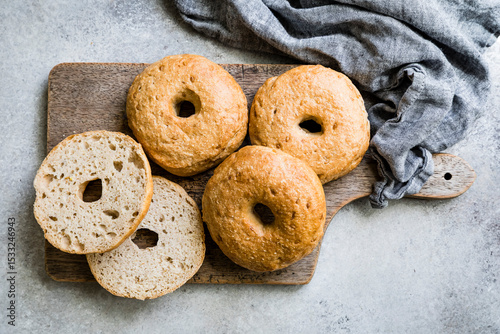 Four whole wheat bagels are placed on a wooden cutting board with a gray cloth beside them.