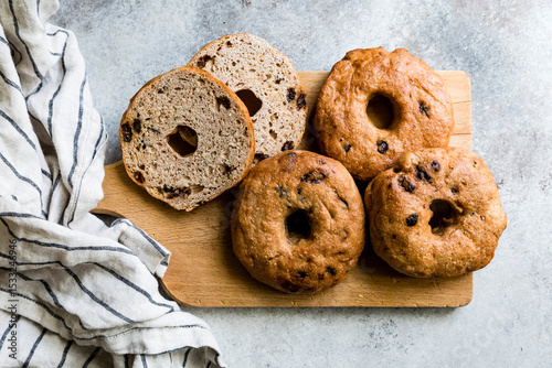 A wooden board with four bagels, three whole and one sliced, next to a striped kitchen towel.