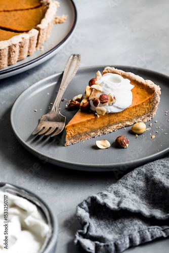 A slice of pumpkin pie topped with whipped cream and nuts on a gray plate with a fork.