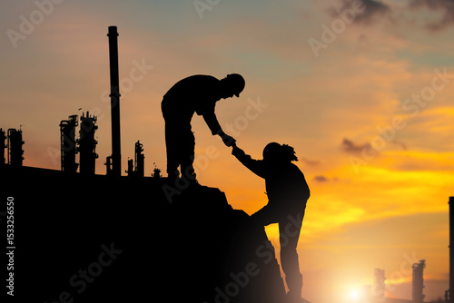Canvas Print Silhouettes of Two workers helping each other up a hill with factory background,