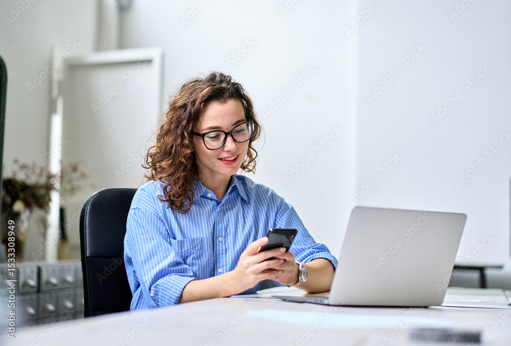 Fototapeta premium Busy young happy business woman, smiling professional businesswoman worker looking at smartphone using cellphone mobile technology apps working or in office checking cell phone sitting at desk.