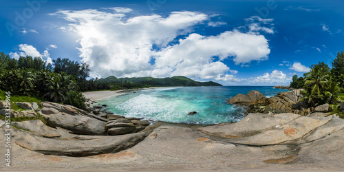 Pristine beach with turquoise waves crashing against rocky cliffs, surrounded by lush green vegetation under a clear blue sky. Police Bay. Mahe, Seychelles. VR 360.