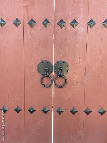 Traditional Korean wooden door with metal decorative studs and ring handles in pink wood.
