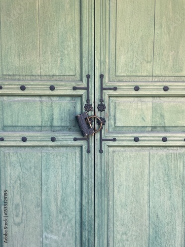 Vintage green wooden door with ornate iron lock and decorative metal studs.
