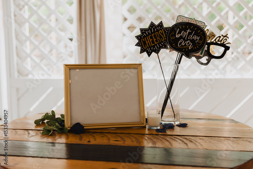 Fun wedding photo booth table setup with blank gold frame, celebration props, and candle on rustic wood table — perfect for parties, receptions, and festive event decor