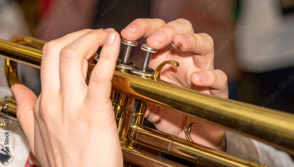 Obraz premium 繊細な指先が輝く真鍮トランペットのバルブを押す瞬間を浅い被写界深度で捉え、手と楽器の細部が鮮明に浮かび上がる美しい一枚