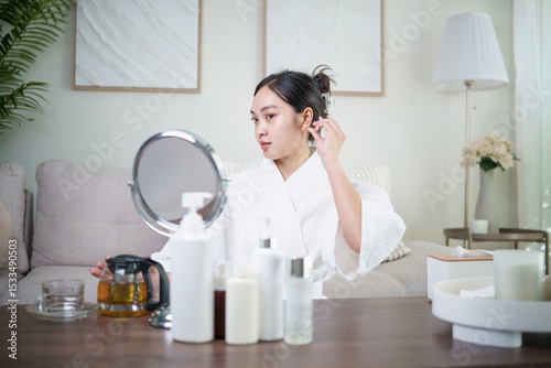 Tableau sur toile Young Asian woman in bathrobe tying her hair before skincare routine at home
