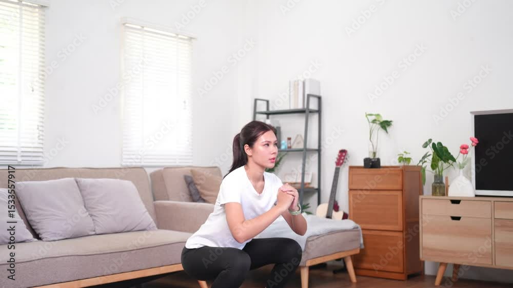 Asian woman doing squat exercises at home, indoor strength training, body toning and fitness for healthy living Asian woman doing squat exercises at home, indoor strength training, body toning and fitness for healthy living