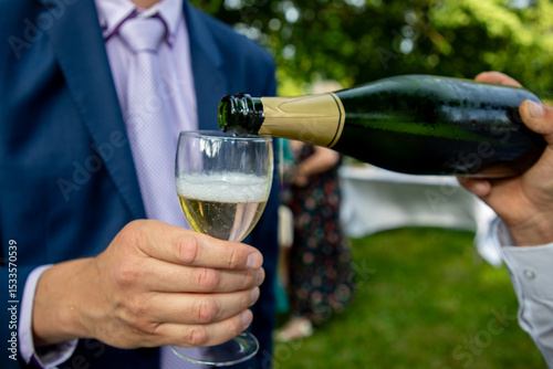 waiter serves a glass of champagne to a man in a suit outdoors on a party day