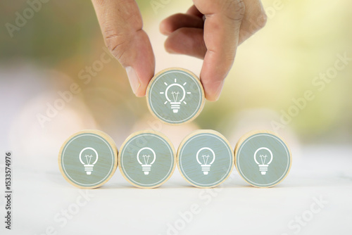Hand chooses wooden toy with light bulb or lamp icons for business growth and human resources or leadership and creativity thinking idea motivation or vision and knowledge learning.