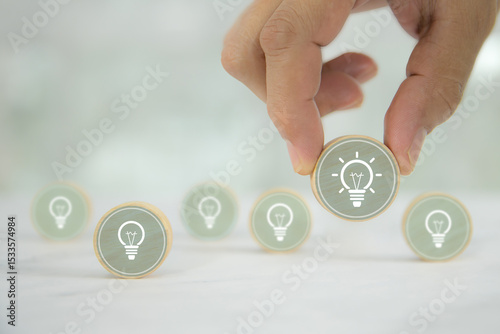 Hand chooses wooden toy with light bulb or lamp icons for business growth and human resources or leadership and creativity thinking idea motivation or vision and knowledge learning.