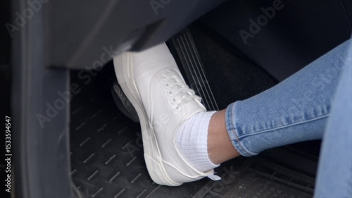Close-up of female legs in stylish sneakers pressing car brake pedal, while woman driver driving vehicle in city traffic.
