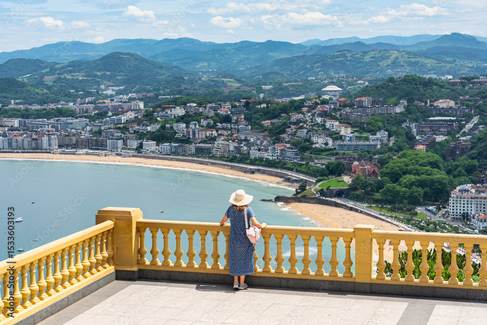 Obraz premium Tourist woman leaning out of a large balcony with stunning views of the bay of San Sebastian, Basque Country.