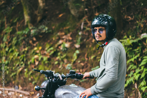 Young man riding a motorcycle in the forest. Biker sitting on a motorcycle.