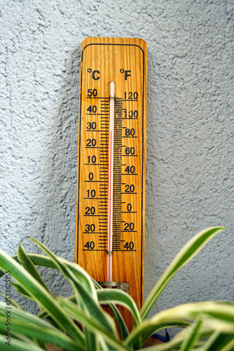 Monitoring indoor and outdoor temperatures: a vertical photo of an analog thermometer on a wooden panel attached to a wall, showing degrees Fahrenheit and Celsius. Uncomfortable conditions in a room