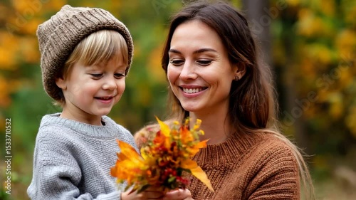 Woman and child in warm sweaters and knitted hat outdoors surrounded by autumn foliage. Bouquet of yellow and orange leaves in hands. Video for family, autumn, parenting, lifestyle 