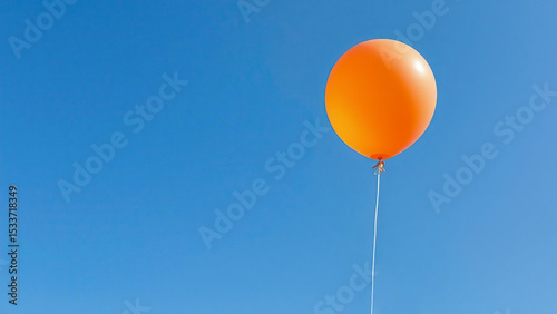 A single orange balloon floats in the clear blue sky. The image symbolizes lightness, freedom and striving upward. Contrasting colors create a bright and minimalistic visual impression.