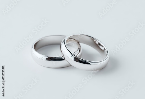 Two polished silver wedding bands rest intertwined on a white background, showcasing their simple, elegant design