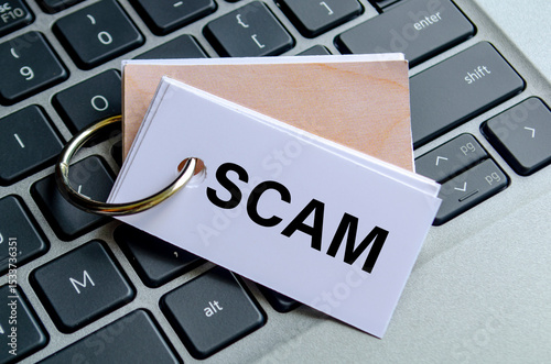 SCAM text on white notepad with laptop keyboard background. Hacker and scam activity concept