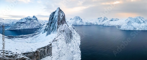 Segla in Norwegen im Winter bei klarer Sicht, markantes Felsmassiv auf der Insel Senja über einer schneebedeckten Fjordkulisse mit umliegenden Bergen im kalten Abendlicht