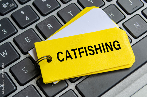 Catfishing text on white notepad with laptop keyboard background. Hacker and scam activity concept