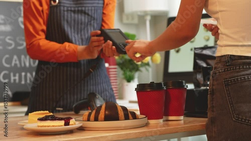 A young Asian female barista in modern cafe assists woman customer ordering latte, fresh coffee beans, dark roast, croissant, completing the purchase with mobile payment at the POS using QR code.