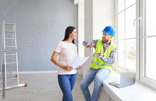 Young woman homeowner discussing design project or repair of new apartment with foreman standing in empty room. Meeting with builder about interior decoration or home layout. Moving concept.