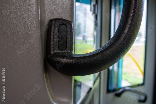 Black handle on a bus door. The handle is black and has a silver knob. The handle is attached to the door and is used to open and close the door