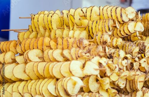 Golden spiral-cut potatoes threaded on wooden skewers. Appetizing display of crispy street food. The accordion-style sliced potatoes showcase perfect knife work and mouth-watering texture.
