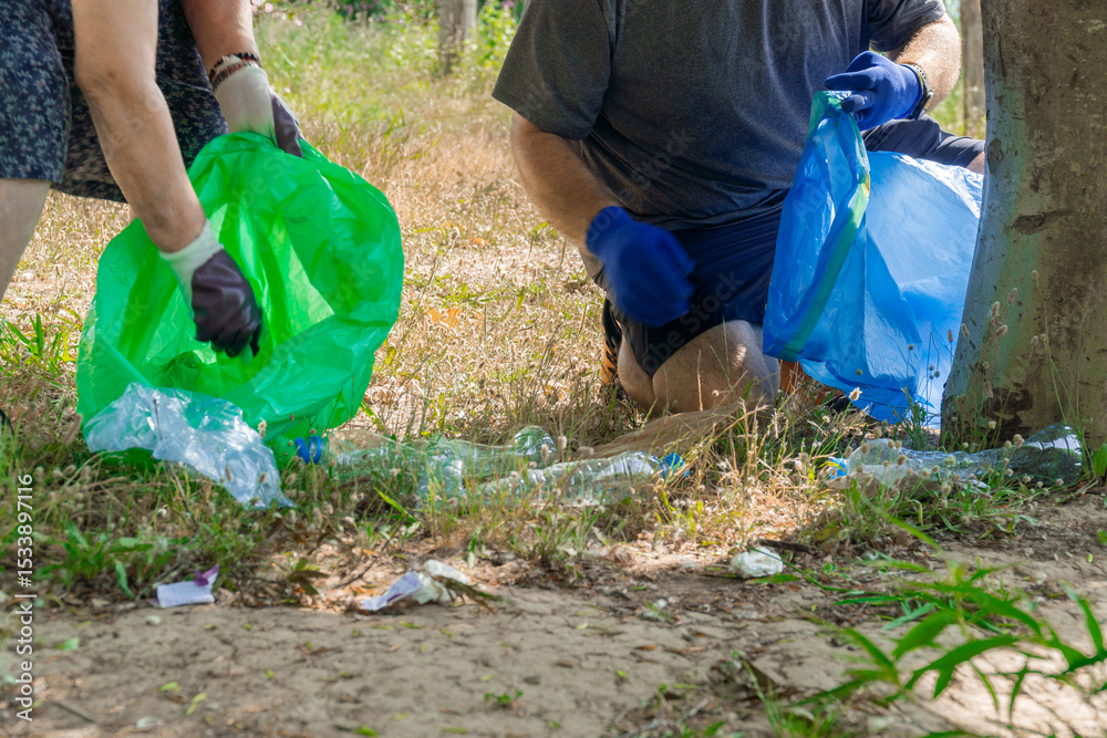 Naklejka premium One man and a senior woman as a volunteers cleaning up a forest, collecting plastic bottles and other garbage in bags.