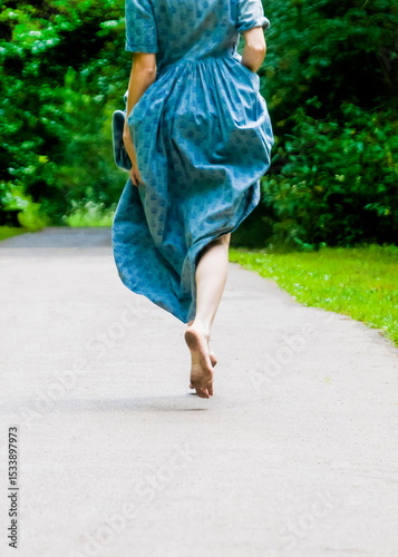 A woman in a blue dress runs barefoot on a path. photo