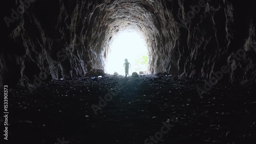 Silhouette of a boy running into a tunnel, framed by bright daylight at the entrance. The contrast of light and darkness evokes a sense of adventure and mystery.