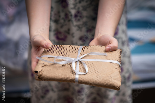 Young woman offering a gift-wrapped book in craft perforated paper with a bow, showcasing thoughtful presentation