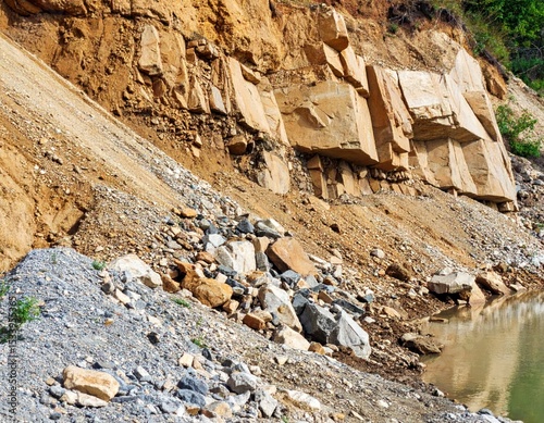 Landslide near a riverbank.  Large blocks of light tan rock,  partially covered by shifting earth and gravel, edge a waterway