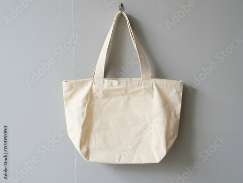 A simple offwhite canvas tote bag hangs from a hook against a muted gray wall