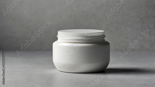 A pristine white jar sits on a gray textured surface, its simple elegance subtly highlighted by the soft light