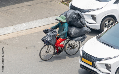 A person is riding a bicycle with full large garbage bags, through an urban street.