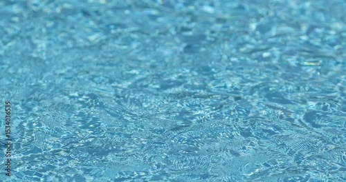 Shallow depth of field details with clear blue and transparent water in a swimming pool during a sunny warm day.