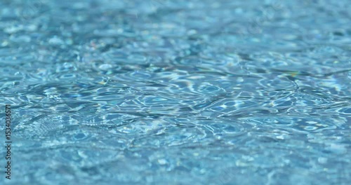 Shallow depth of field details with clear blue and transparent water in a swimming pool during a sunny warm day.